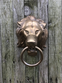 A lion's head, made of aluminum in a brass color, as a door knocker