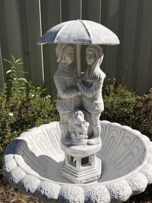 Gartenbrunnen voller Steine mit Kindern unter einem Regenschirm, sehr schön!